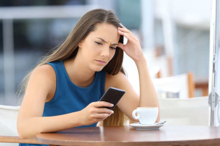 woman with a stressed look looking at cell phone at table
