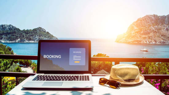 laptop with "booking" on the screen on tropical landscape with hat