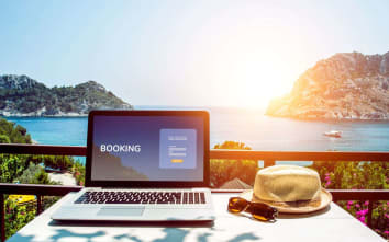 laptop with "booking" on the screen on tropical landscape with hat