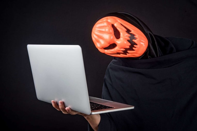 person wearing halloween mask looking at computer