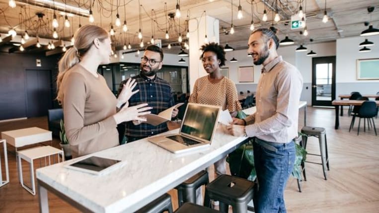 Four-person work team huddled together at a table having a discussion.