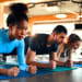 Slim women african american and caucasian ethnicity and muscular man in sportswear doing plank exercise on rubber mat in gym club. The concept of sports and recreation.