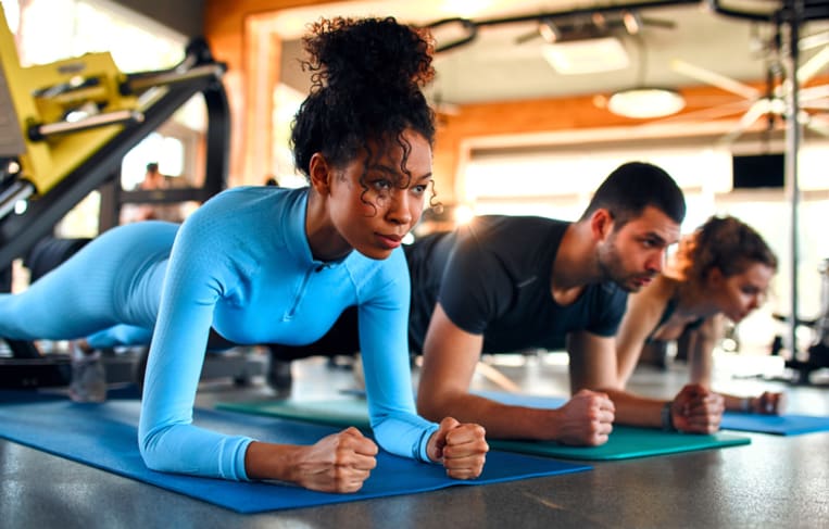 Slim women african american and caucasian ethnicity and muscular man in sportswear doing plank exercise on rubber mat in gym club. The concept of sports and recreation.