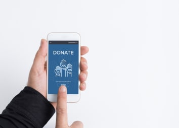 Hands hold a smart phone that reads "donate." One finger hovers over the "donate" button. 