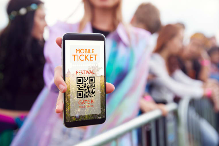 Woman at an outdoor music festival holds up phone showing ticket information