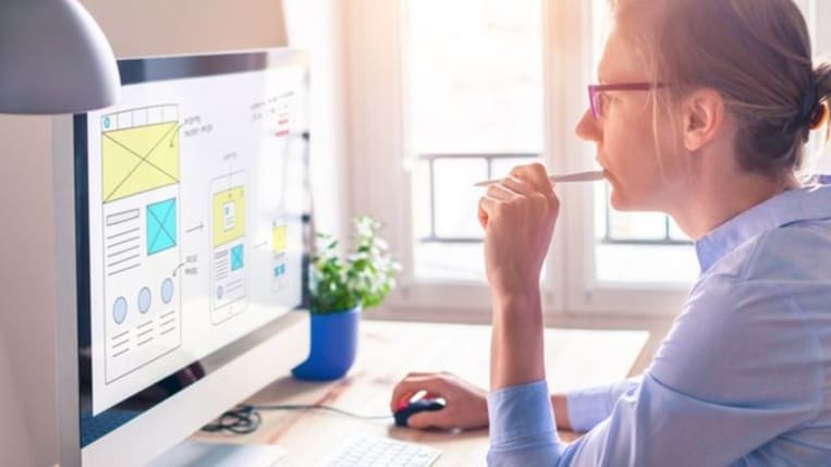 woman wearing glasses sit at computer desk looking at desktop screen