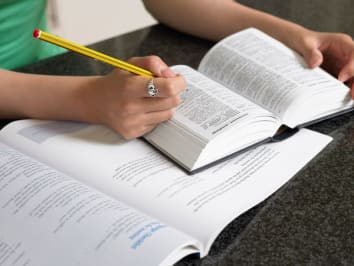 person holding a pencil looking at a dictionary