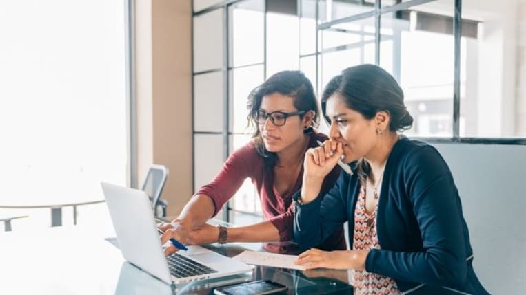 Pair of entrepreneurs sitting at a desk reviewing information on a laptop