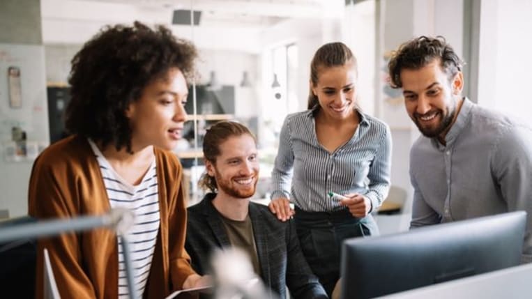 Four office coworkers collaborating at a desktop computer.