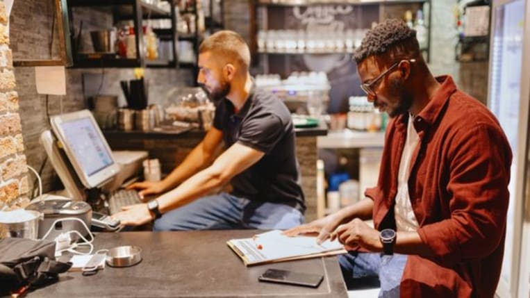 Small business owner and waiter checking their financial records in a cafe
