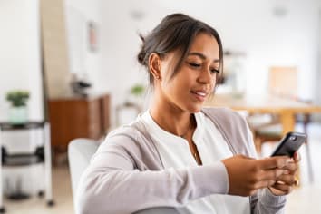 Woman sitting on couch at home using smartphone. 