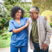 Young woman nurse smiles while putting her arm around an older man. 