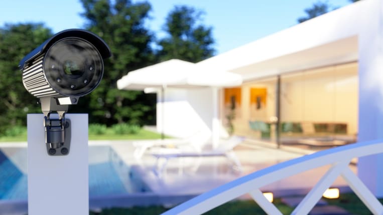 A close-up of a security camera positioned on a fence post outside a house.