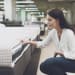A woman in a white shirt and jeans in a mattress store. She examines the mattress she wants to buy. She squats and looks at the mattress�