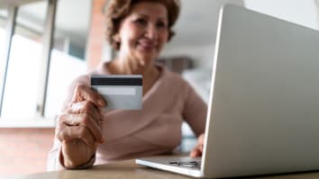 An older woman uses her laptop to shop online. She is holding a credit card.