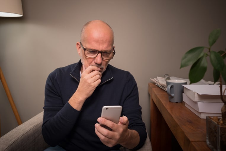 60-something man with glasses, looks skeptically at his smartphone. 