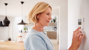 A mature woman adjusts the temperature on a home thermostat.