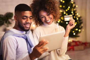 Christmas preparation. Happy black couple buying gifts online, using tablet and credit card