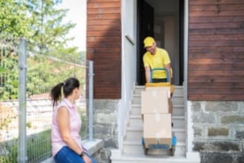 Delivery man in a yellow shirt and hat pushing a dolly piled with boxes