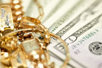 Close up photo of gold jewelry laid next to U.S. currency, specifically a pile of fifties and twenties.