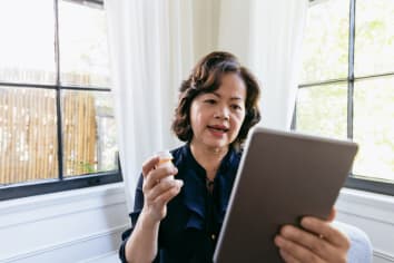Woman holding up a prescription bottle and speaking with her doctor on her tablet