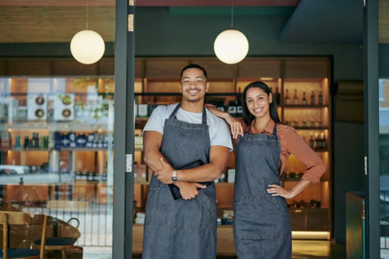 Smiling young deli owners standing at their store entrance