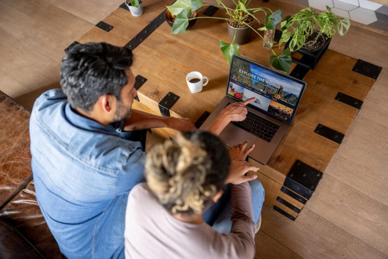 Happy couple at home booking a trip online using their laptop computer 