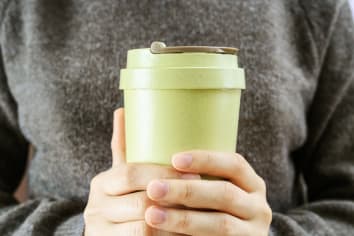Girl holds in her hands reusable coffee cup. Take away big mug for drinks.