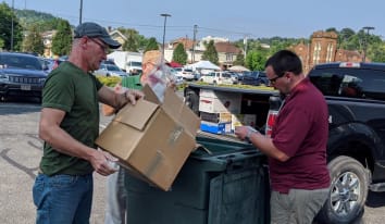 two male volunteers dumping documents from a cardboard box into a bin to be shredded
