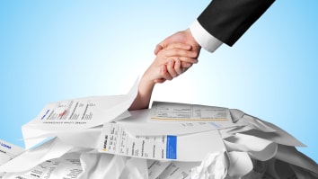 A person wearing a business suit extends their hand to pull someone else out from under a pile of unpaid bills.