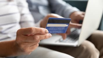 Fingers holding plastic credit card on background computer on husband lap top