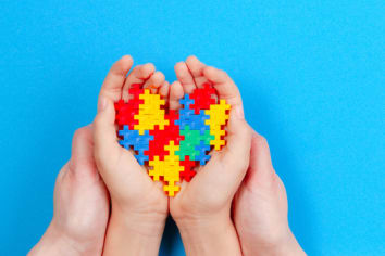 Adult and kid hands holding colorful heart on blue background. World autism awareness day concept.�