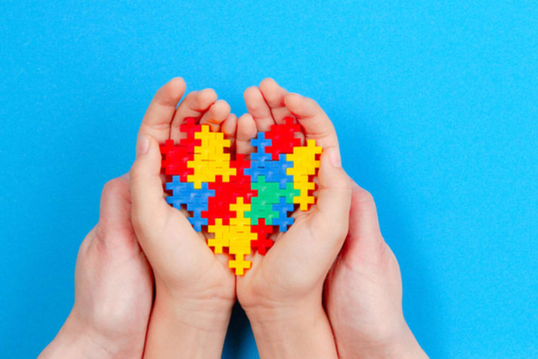 Adult and kid hands holding colorful heart on blue background. World autism awareness day concept.�