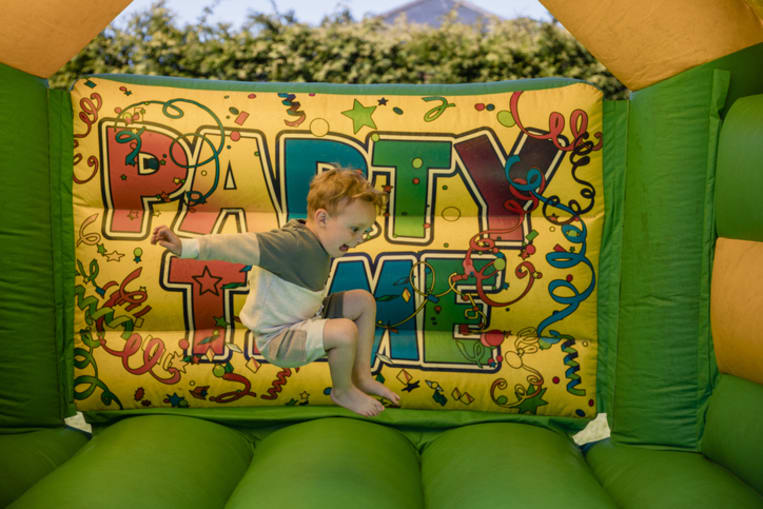 Boy jumps in a bouncy house in front of a sign reading "party time." 
