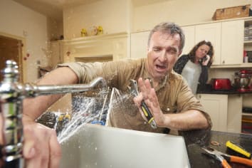 woman calling a plumber burst pipes spraying on man in kitchen
