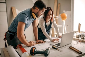 couple looking at blue prints for home with power tools and computer