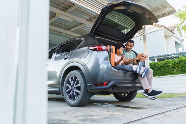 Cheerful Black African American father and son playing sitting in car trunk before a move.