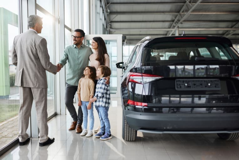 Happy family came to a successful agreement with salesperson while buying a car in a showroom.