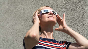 A person wearing protective solar eclipse glasses looks up at the sun.