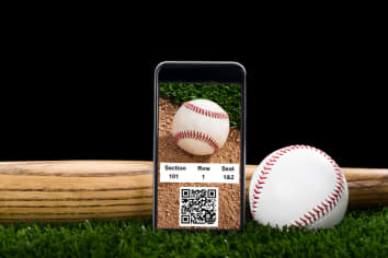 A Smart Phone displaying online baseball tickets with QR code, sitting on the turf with a baseball, glove and bat against a night sky. 