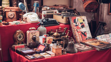 A collection of vintage items on a table for sale, including vinyl records, a corded telephone, a typewriter and a clock.