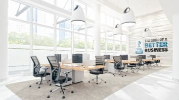 A meeting room with desks, chairs, and computers; one outside wall is all glass and at the far end of the room on the wall is the Accredited Business Seal, and it says The Sign of A Better Business