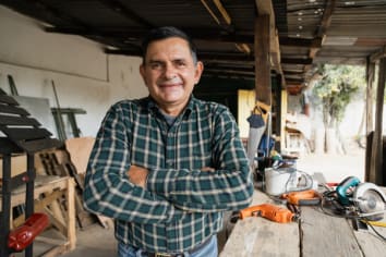 Hispanic carpenter smiling proud in wood shop of him - Proud owner of carpentry shop standing with arms crossed