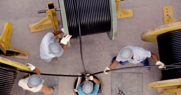 Overhead view of four electricians unwinding three large spools of wiring for electrical work