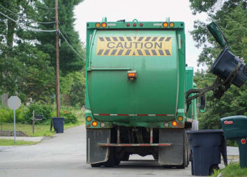 A garbage truck uses a mechanical arm to collect trash in a residential neighborhood.