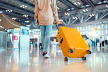 Young female traveler passenger walking with a yellow suitcase at the modern Airport Terminal, Woman on her way to flight boarding gate, Ready for travel or vacation journey