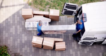 two moving professionals in blue shirts moving furniture and boxes out of moving van