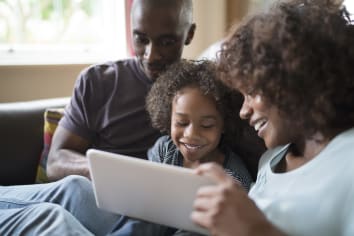 african american parents sitting with young child looking at white tablet on couch
