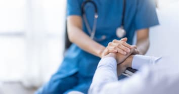 Medical professional wearing stethoscope and blue scrubs is holding hands of patient