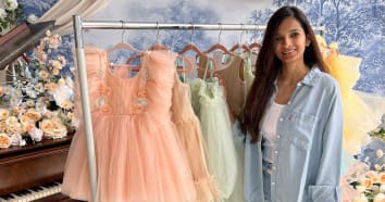 Owner of Happy Lilliput standing next to hanger with peach, yellow, and green children's tulle and floral dresses